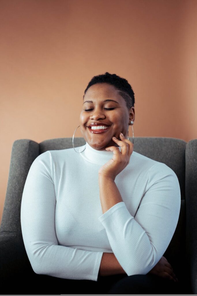 A close-up shot of a smiling woman in a white sweater, sitting indoors.