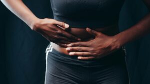 Close-up of a person pressing hands on abdomen, indicating discomfort or pain, against a black background.