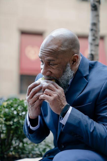 Elderly man in a suit enjoying a sandwich during breaktime outdoors.